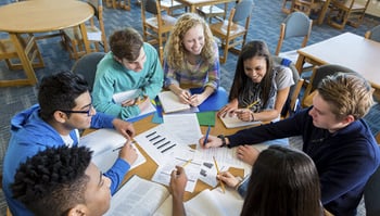 students working on assignment at table covered in project papers 